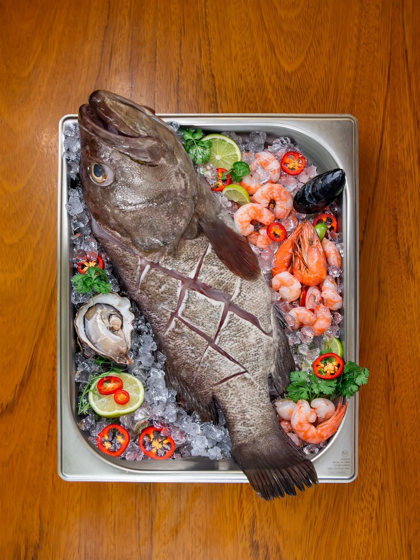 Pescado fresco entero sobre hielo con langostinos, ostras y limones